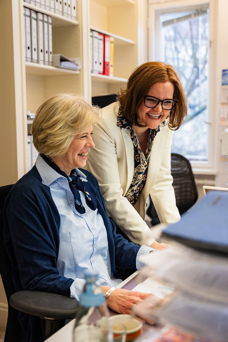 Zwei Mitarbeiterinnen lachen und arbeiten gemeinsam.